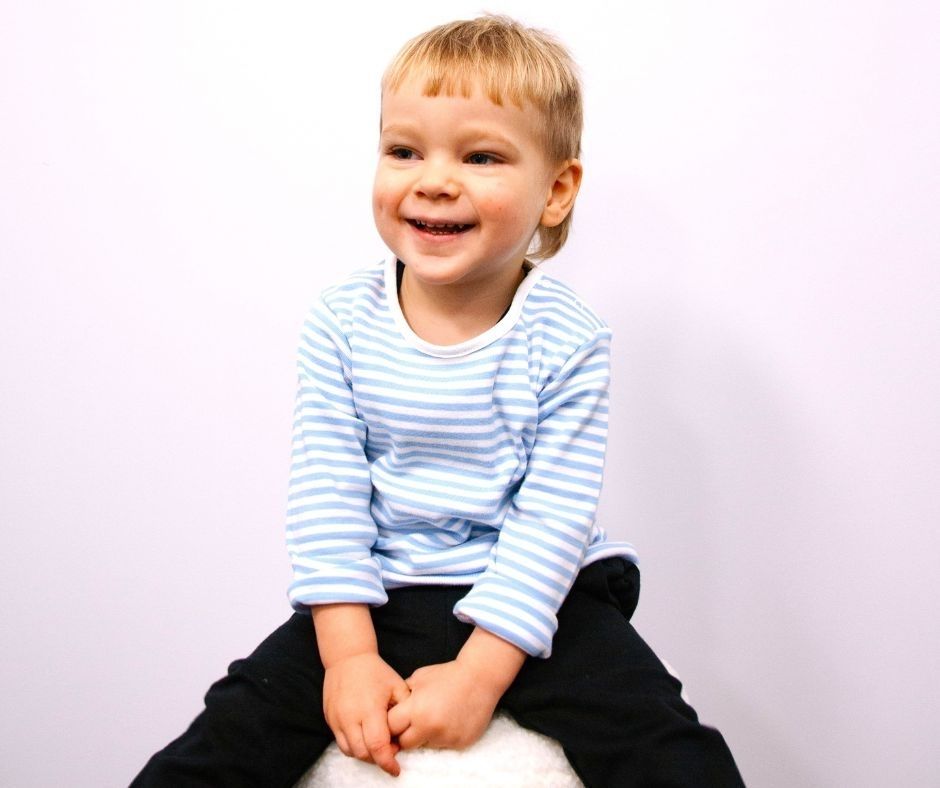 Child wearing a blue and white striped shirt sitting on a white surface with a plain background