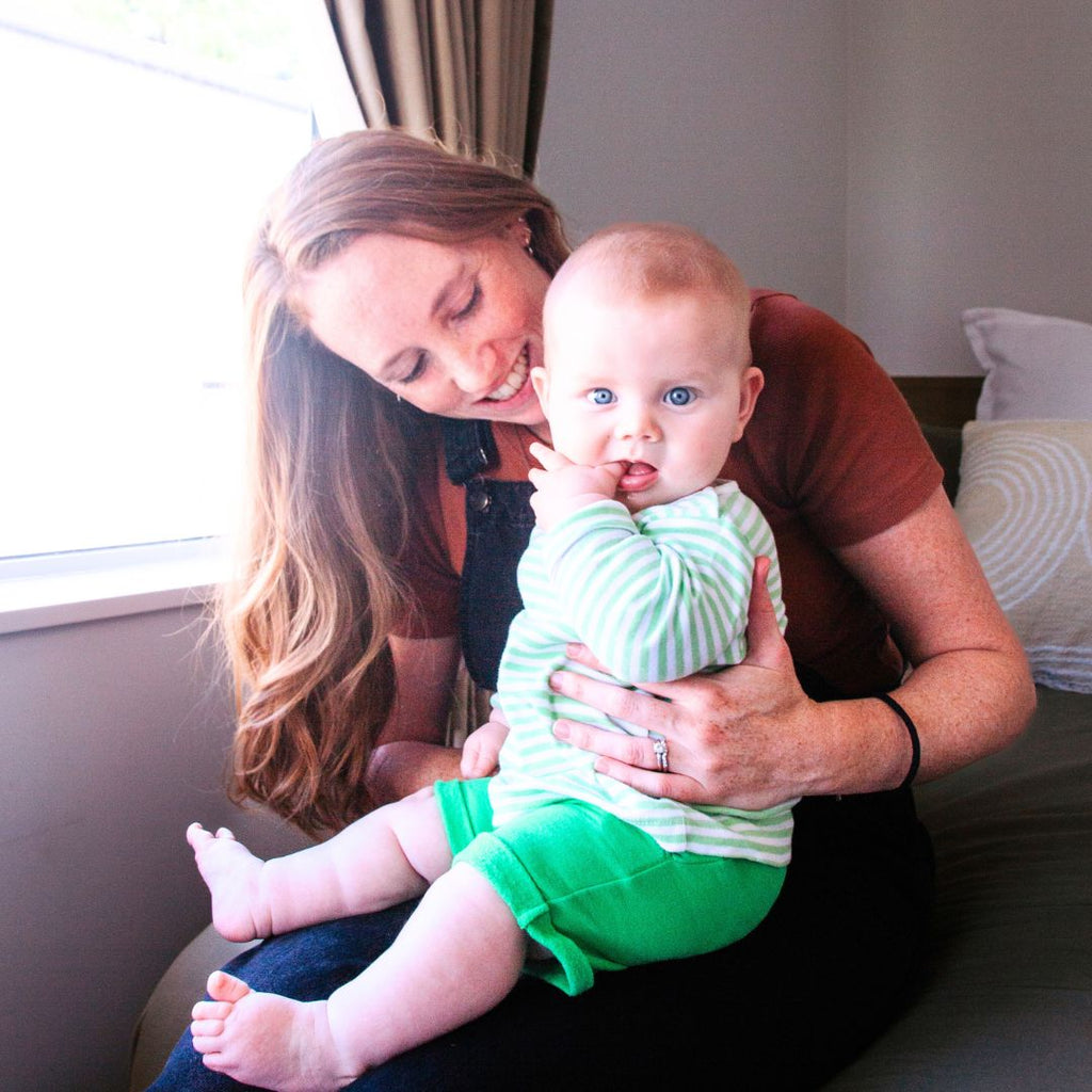 Woman holding a baby in a room with a window and pillows.