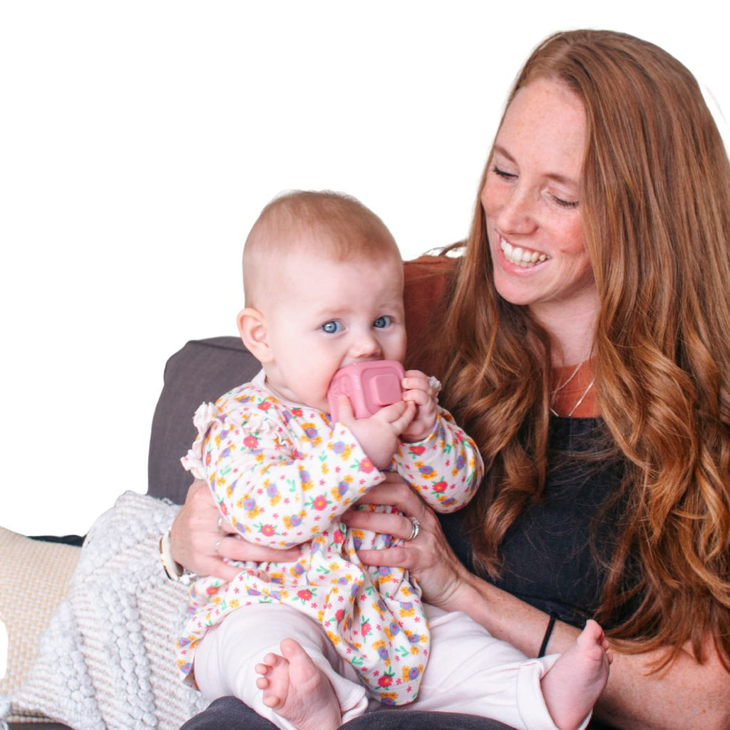 Woman holding a baby with a pink teething toy on a white background
