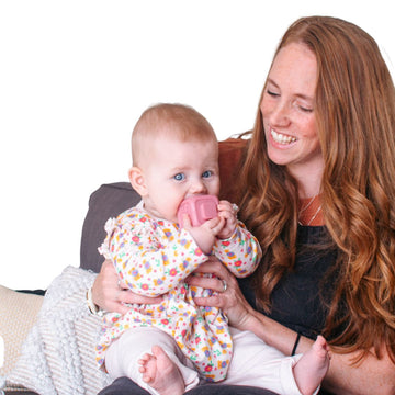 Woman holding a baby with a pink teething toy on a white background